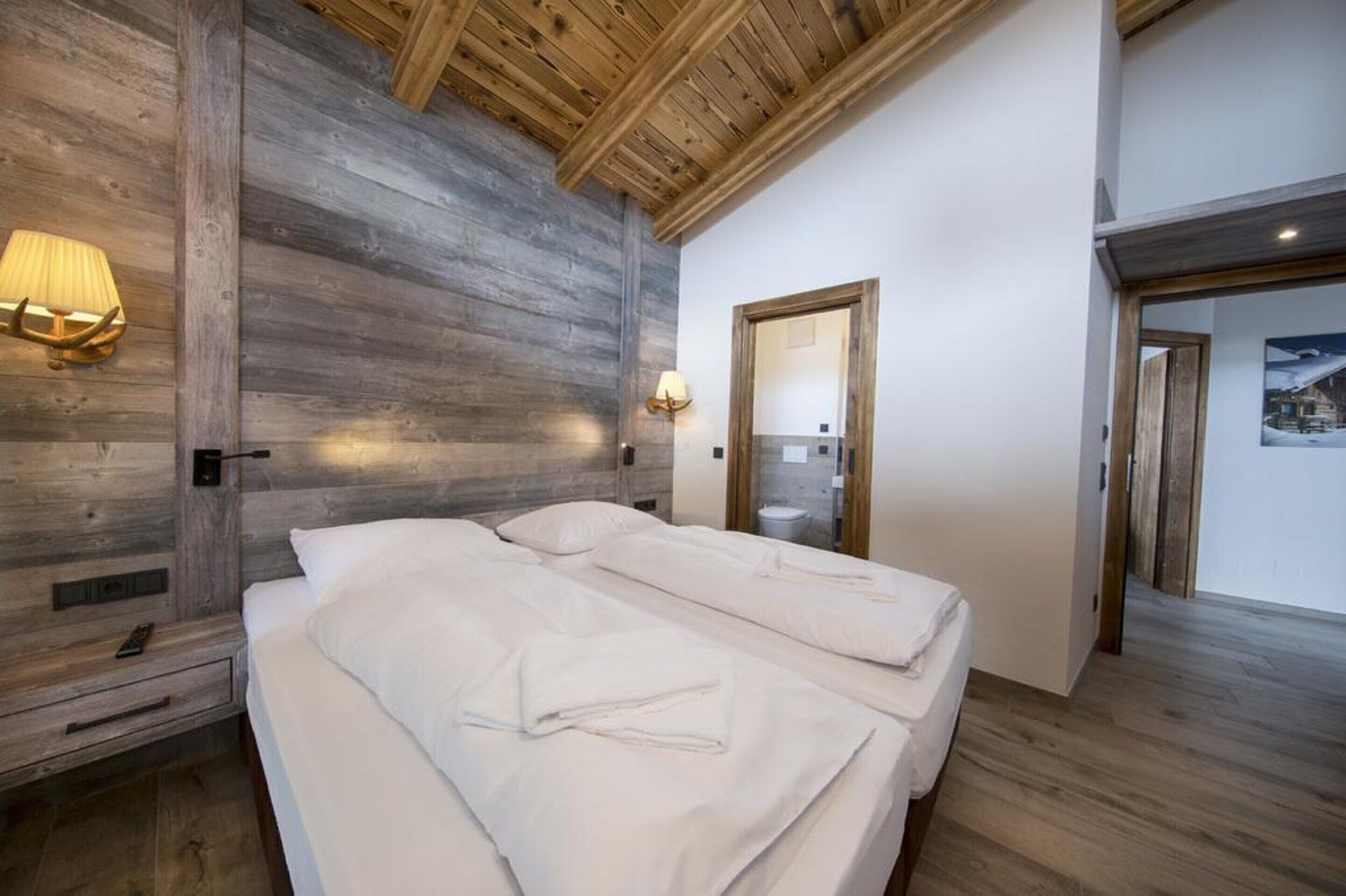Ein Schlafzimmer mit zwei Betten, Holzbalken an der Decke, einer Holzwand und einem Spiegel.