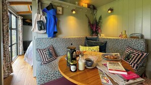 A cozy cabin interior with a wooden table, a sofa with patterned cushions, and a bookshelf with various items. - The Drey, a Stunning Cumbrian Shepherd’s Hut (Carnforth)