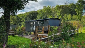 A rustic cabin with a wooden deck and a small garden area. - The Drey, a Stunning Cumbrian Shepherd’s Hut (Carnforth)