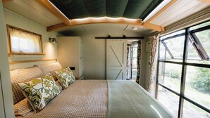A cozy bedroom with a bed, a window, and a door. - The Drey, a Stunning Cumbrian Shepherd’s Hut (Carnforth)