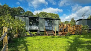 A metal building with a large window and a wooden staircase leading to a door. - The Holt, a Stunning Cumbrian Shepherd’s Hut (Carnforth)