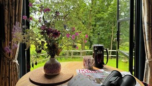 A round wooden table with a floral vase, a magazine, binoculars, and a mug. - The Sett, a Stunning Shepherd’s Hut & Hot Tub (Carnforth)