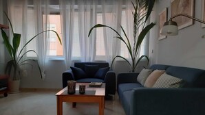 A living room with a blue sofa, a wooden coffee table, and two potted plants.