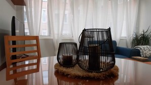 A modern living room with a glass table, two black wireframe lamps, a wooden chair, and a blue sofa.