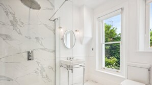 Ein Badezimmer mit Dusche, Waschbecken, Toilette und einem Fenster mit Blick ins Grüne.