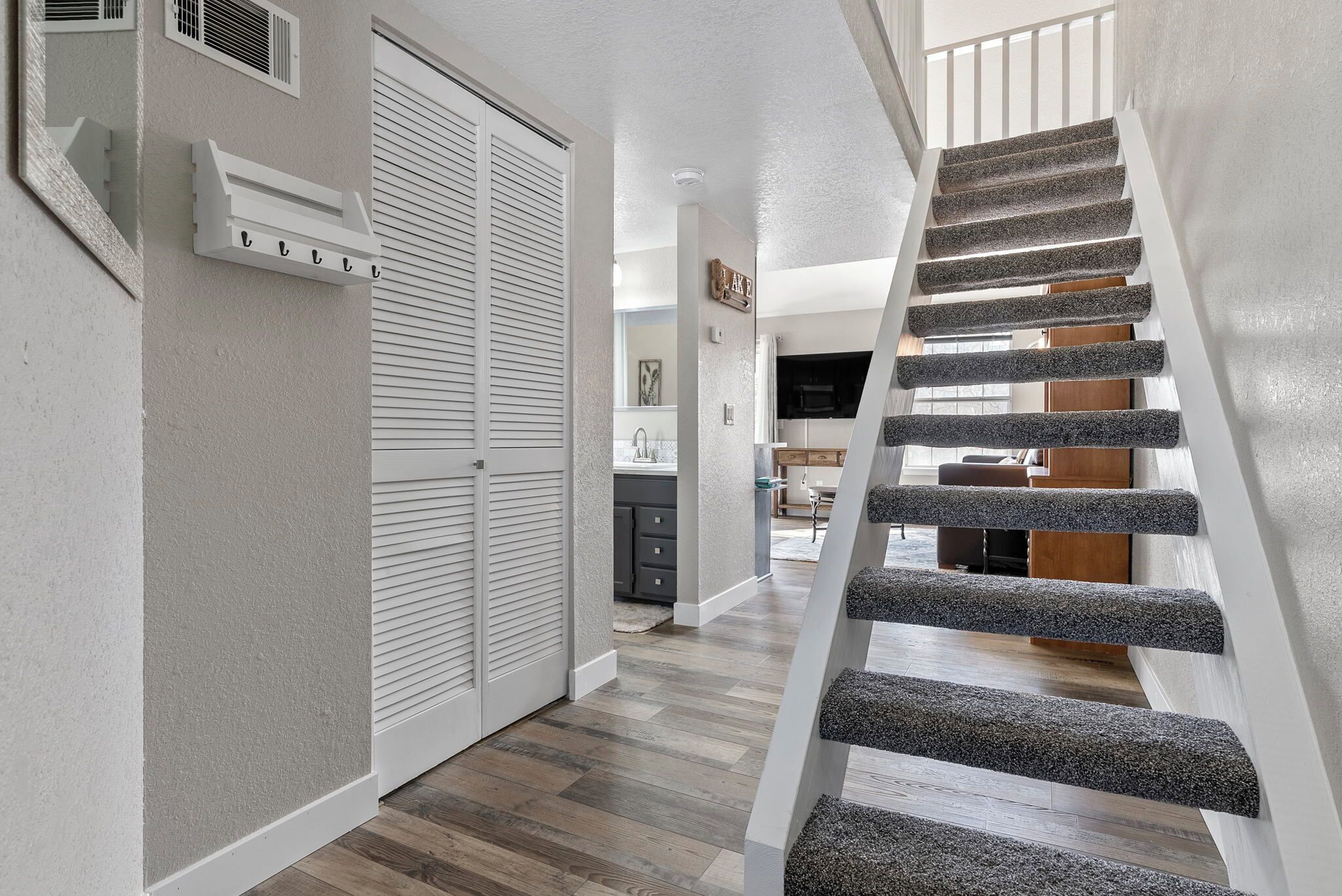 Un interior moderno con una escalera, piso de madera y una cocina visible al fondo.