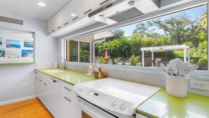 Eine moderne Küche mit einem großen Fenster, weißen Schränken, einer grünen Arbeitsplatte und einem eingebauten Backofen.