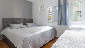 A bedroom with a large bed, a smaller bed, a window with curtains, and a thermostat on the wall. - Condomínio Praia de Taormina (Guaruja)