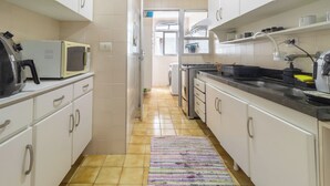 A narrow kitchen with white cabinets, a microwave, a stove, and a sink. - Condomínio Praia de Taormina (Guaruja)