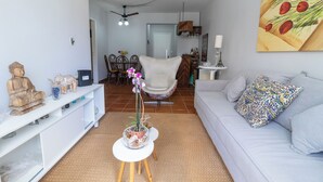 A living room with a sofa, a white console table, a decorative plant, and a dining area in the background. - Condomínio Praia de Taormina (Guaruja)