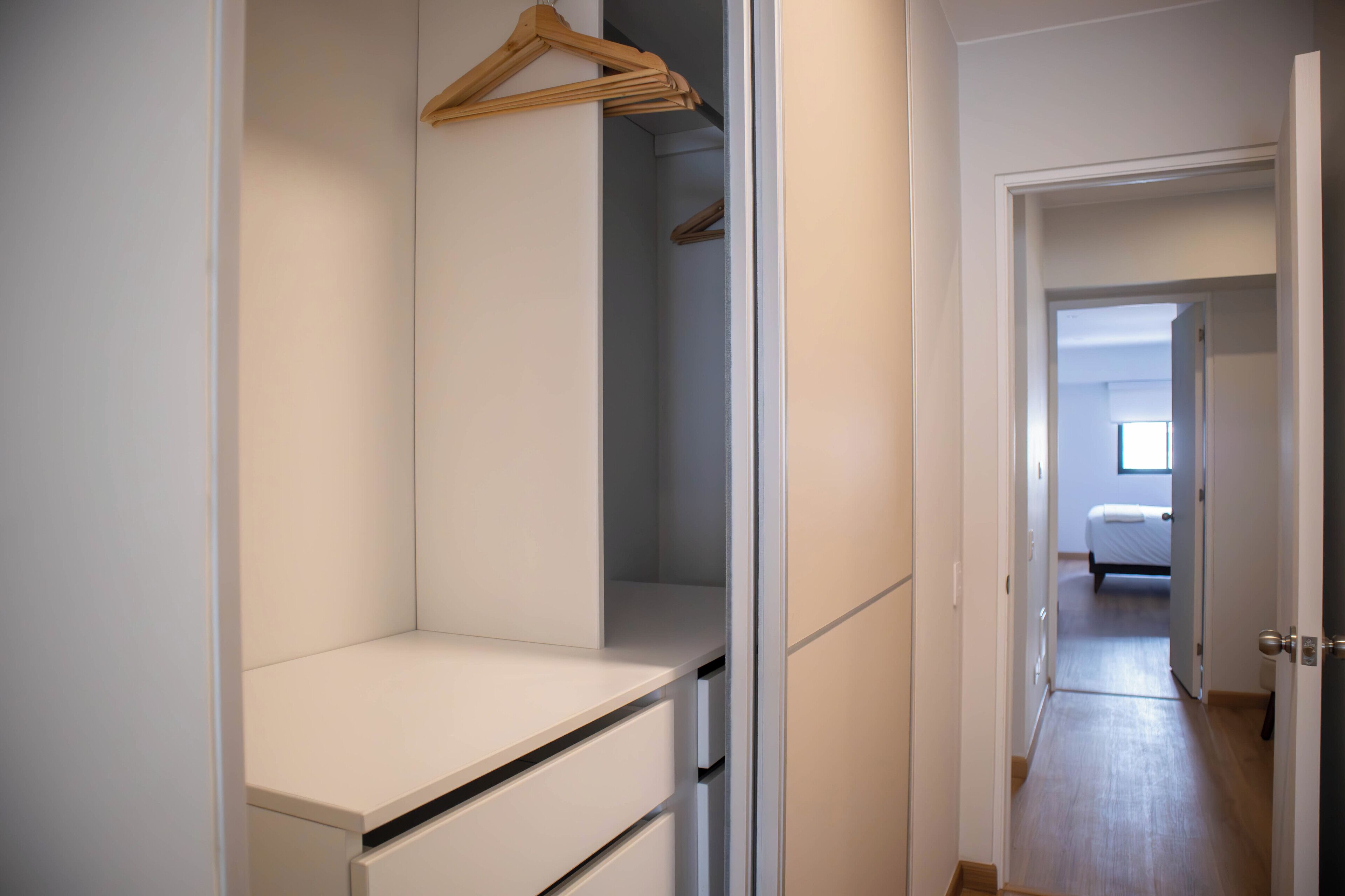 A hallway leading to a bedroom with a bed, a closet with hanging clothes, and a door to another room.