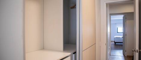 A hallway leading to a bedroom with a bed, a closet with hanging clothes, and a door to another room.
