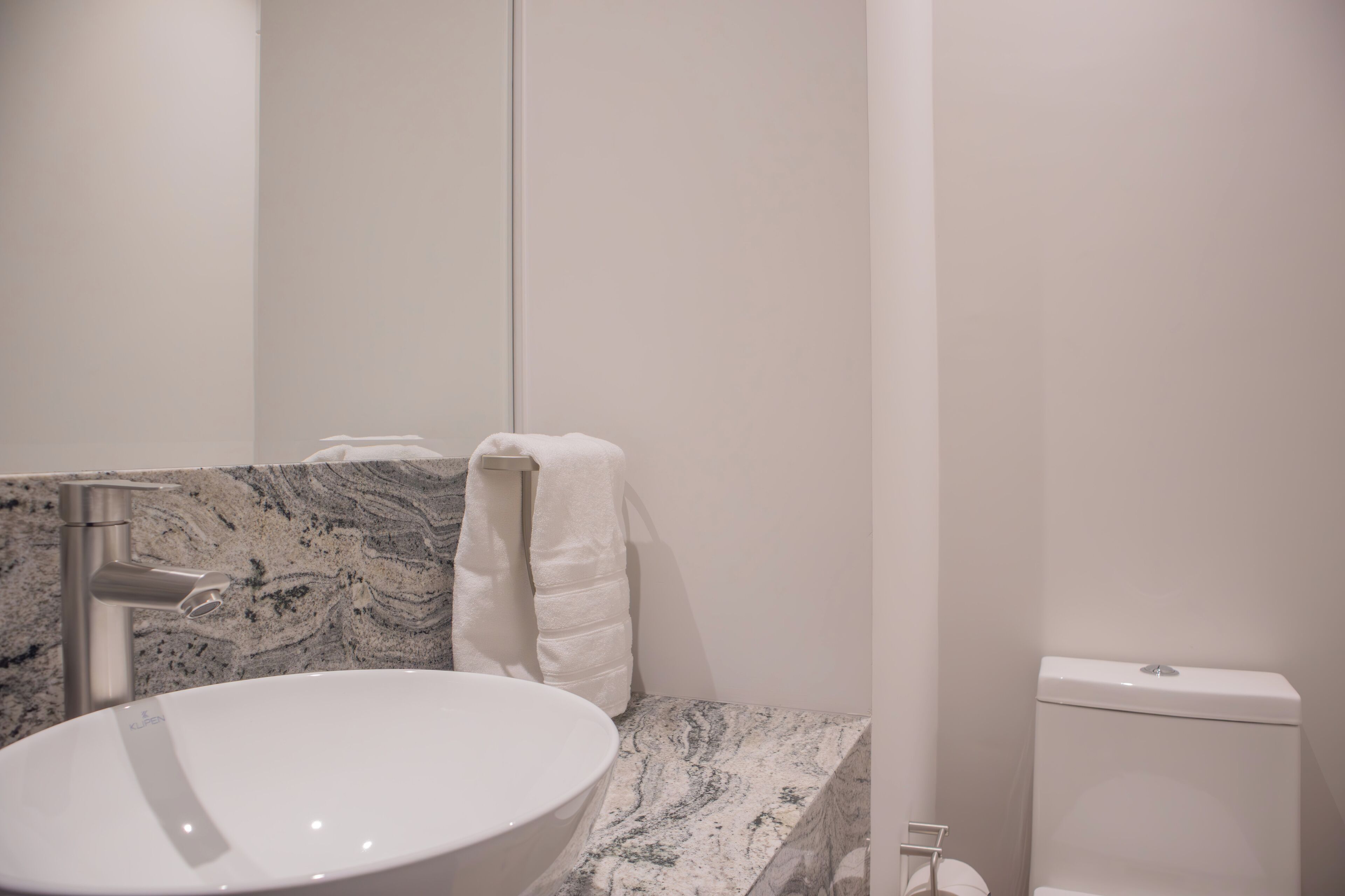 A bathroom with a white sink, a marble countertop, a towel rack, and a toilet.