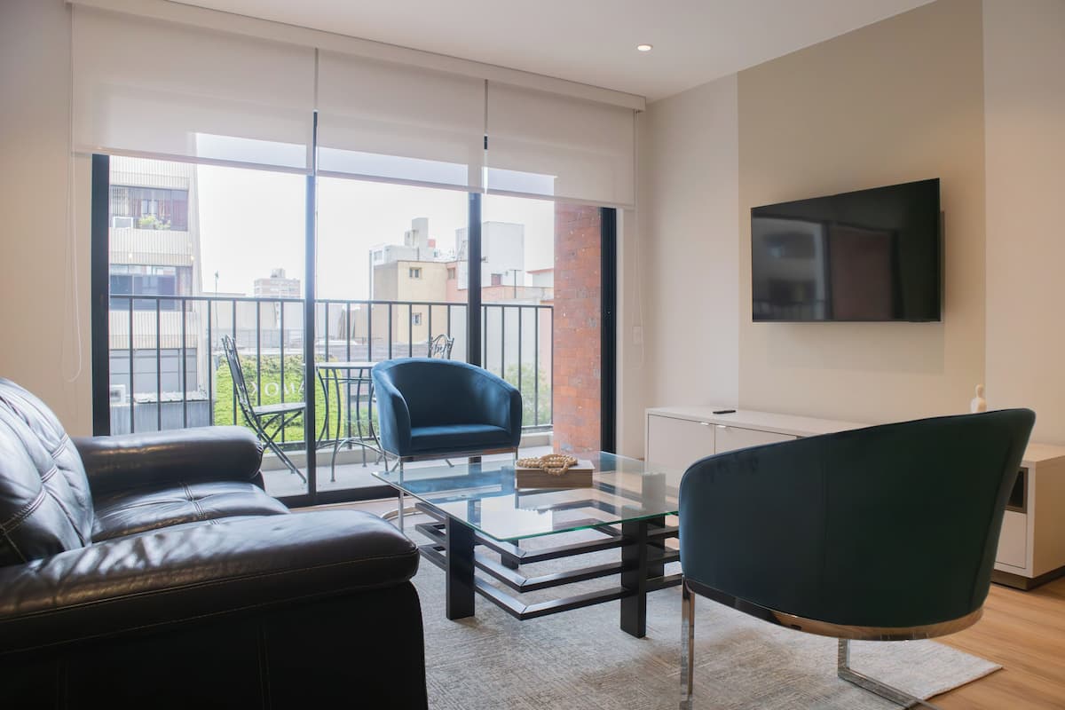 A modern living room with a glass coffee table, leather sofa, and a TV mounted on the wall.