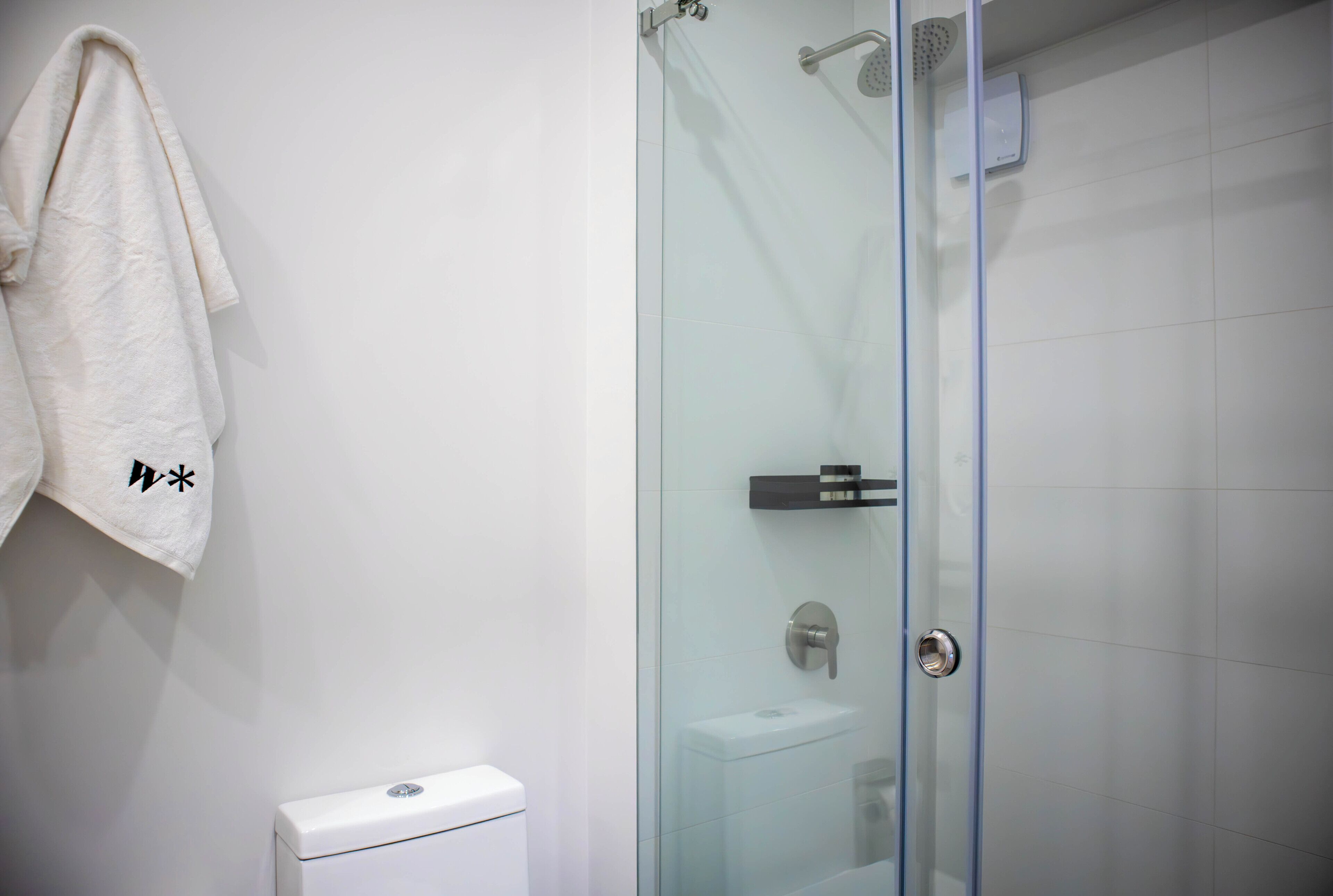 Un baño con cabina de ducha de vidrio, inodoro blanco y una toalla colgada en la pared.