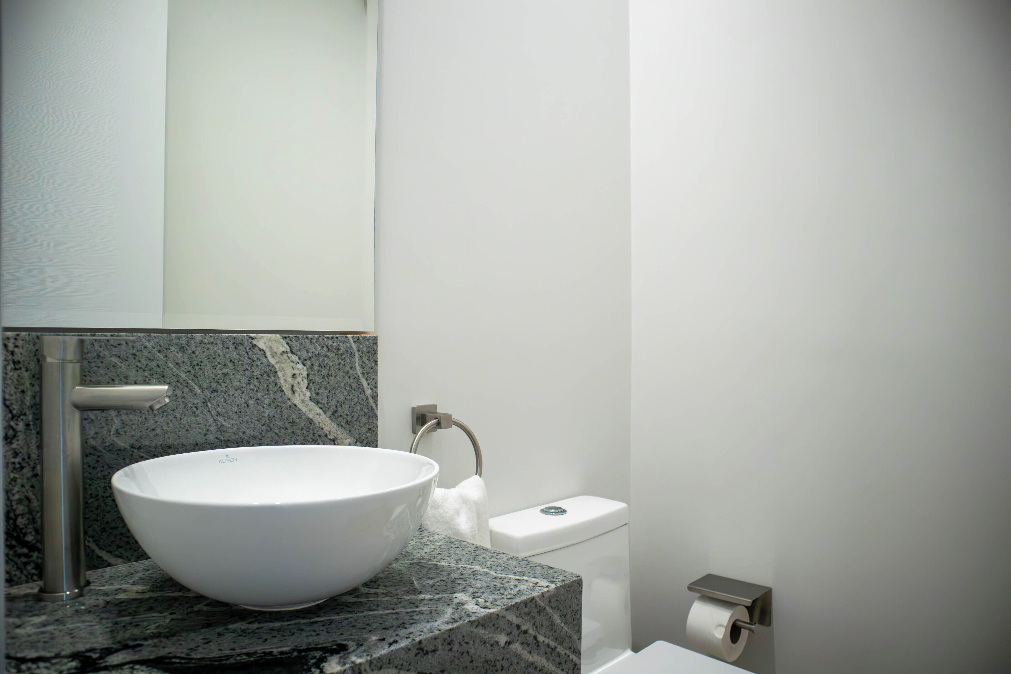 Een badkamer met een wit wastafel, een marmeren aanrecht, een toilet en een handdoekdispenser.