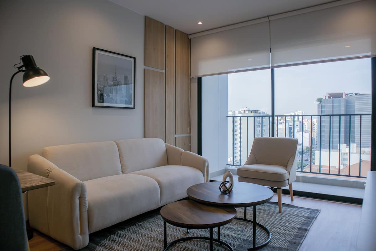 A modern living room with a sofa, two side tables, a chair, and a large window with a city view.