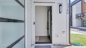 Entrada de un edificio moderno con puerta de vidrio, un escalón pequeño que conduce al interior y un buzón en la pared.