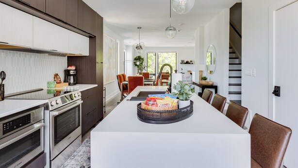 Una cocina moderna con electrodomésticos integrados, un comedor con una isla central, y una escalera que lleva a otro nivel.