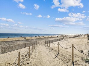 A beach with a wooden fence and rope barrier, sandy beach, and the ocean in the background.