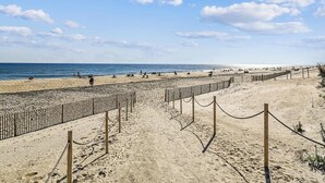 Una playa con una cerca de madera y una barrera de cuerda, arena y el océano al fondo.