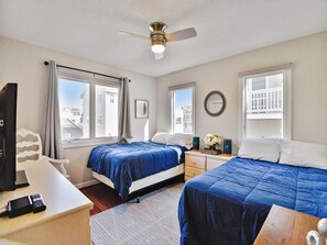 Habitación de hotel con dos camas, un escritorio, una silla, ventilador de techo y ventanas amplias.