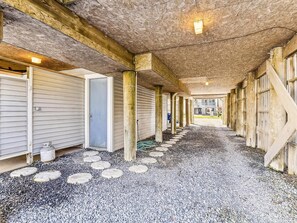 Un corredor exterior cubierto con un camino de grava, columnas de madera y una serie de puertas a un lado.