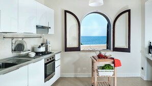 A modern kitchen with white cabinets, a stainless steel sink, and a view of the sea through arched windows. - Marina dei Greci (Giardini Naxos)