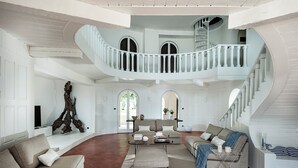 A spacious living area with a high ceiling, a central seating arrangement, and a staircase leading to an upper level. - Marina dei Greci (Giardini Naxos)