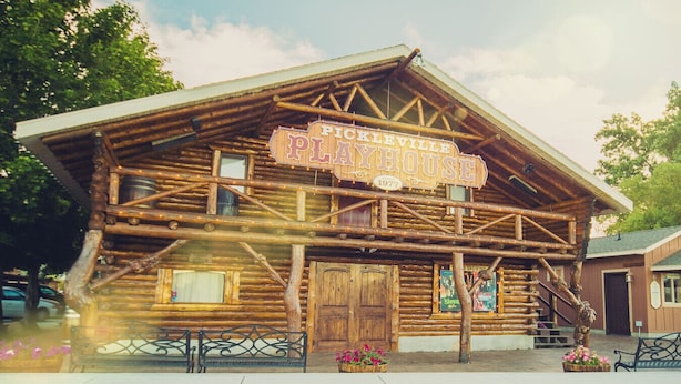 A rustic log cabin with a sign reading "Pickleville Playhouse 1977".