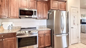 A kitchen with wooden cabinets, a stainless steel refrigerator, a microwave, an oven, and a granite countertop.