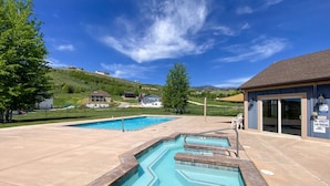 A swimming pool area with two pools, a spa capacity sign, and a building with a roof.