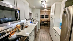 A modern kitchen with stainless steel appliances, a wooden floor, and a dining area with a chandelier.