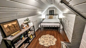 A compact, modern bedroom with a bed, bedside tables, a small rug, and a framed picture on a shelf.
