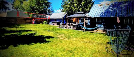 A backyard with a hammock, a basketball hoop, and a house with a metal roof.