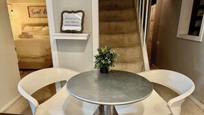 A dining area with a round table and two white chairs, a small potted plant, a framed welcome sign, and a staircase in the background. - Downtown SLC 1BR · Marmalade · Walk to Capitol (Salt Lake City)