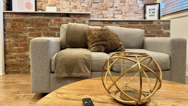 A living room with a grey sofa, a brown throw blanket, and a decorative golden sphere on a wooden coffee table. - Downtown SLC 1BR · Marmalade · Walk to Capitol (Salt Lake City)