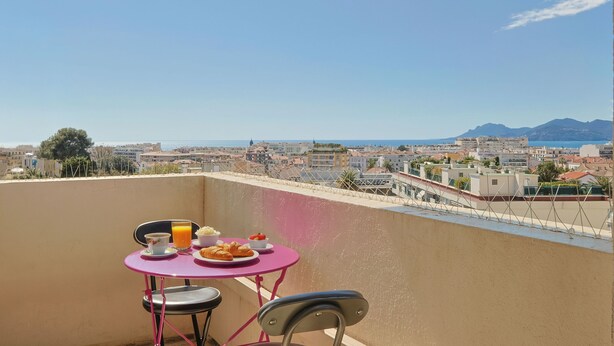 A balcony with a table and chairs, overlooking a cityscape with buildings and mountains in the distance. - L Horizon in Cannes With 2 Bedrooms and 1 Bathrooms (Cannes)