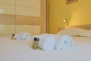 A neatly made bed with rolled white towels and a bottle of lotion, a bedside lamp, and a wooden headboard in a hotel room. - L Horizon in Cannes With 2 Bedrooms and 1 Bathrooms (Cannes)