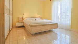 A bedroom with a wooden bed, a nightstand, a drawer, and a window with sheer curtains. - L Horizon in Cannes With 2 Bedrooms and 1 Bathrooms (Cannes)