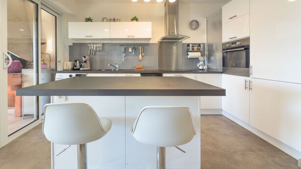 Una cucina moderna con isola centrale, mobili bianchi, elettrodomestici in acciaio inossidabile e un'ampia finestra.