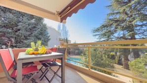 Un balcone con un tavolo apparecchiato per due, una piscina e vista su alberi e un edificio.
