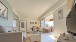 Un soggiorno moderno con divano, tavolino e televisore. C'è una zona pranzo con tavolo e sedie, e un balcone con vista.