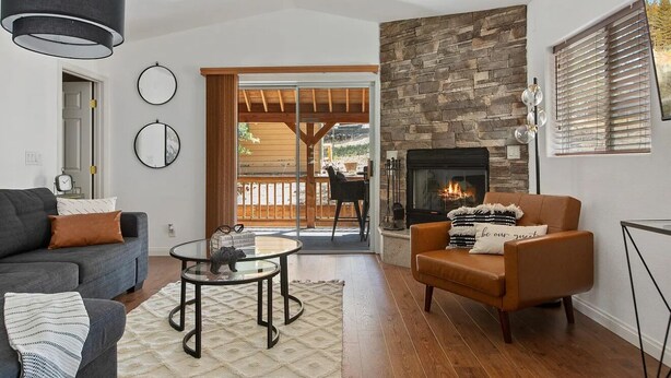 A living room with a fireplace, a sofa, a coffee table, and a view of the outdoors. - Cozy Cabin, A/C, Hot Tub, Tankless Water Heater, Jacuzzi, Full Kitchen (Big Bear Lake)