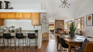 A modern kitchen with wooden cabinets, a bar area, and a dining space with a large wooden table and chairs. - Cozy Cabin, A/C, Hot Tub, Tankless Water Heater, Jacuzzi, Full Kitchen (Big Bear Lake)