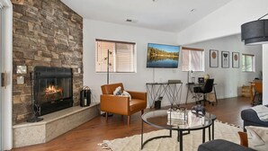 A spacious living room with a stone fireplace, comfortable seating, a flat-screen TV, and a view of the outdoors. - Cozy Cabin, A/C, Hot Tub, Tankless Water Heater, Jacuzzi, Full Kitchen (Big Bear Lake)