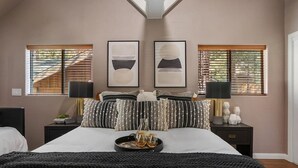 A bedroom with a large bed, two bedside tables, a nightstand, a window with blinds, and two framed artworks on the wall. - Cozy Cabin, A/C, Hot Tub, Tankless Water Heater, Jacuzzi, Full Kitchen (Big Bear Lake)