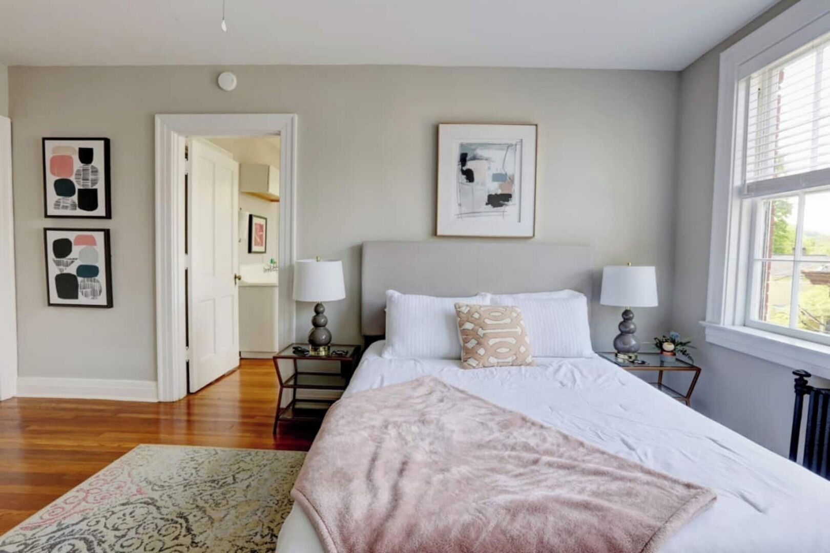 Une chambre à coucher avec un grand lit, deux tables de chevet, une commode, une fenêtre et des œuvres d’art accrochées aux murs.