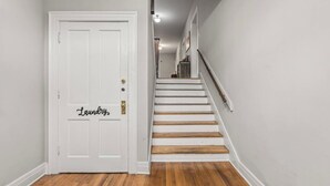 A hallway with a white door labeled "Laundry" and a wooden staircase. - Historic Building/Walkable to Dtown/Central (Frankfort)