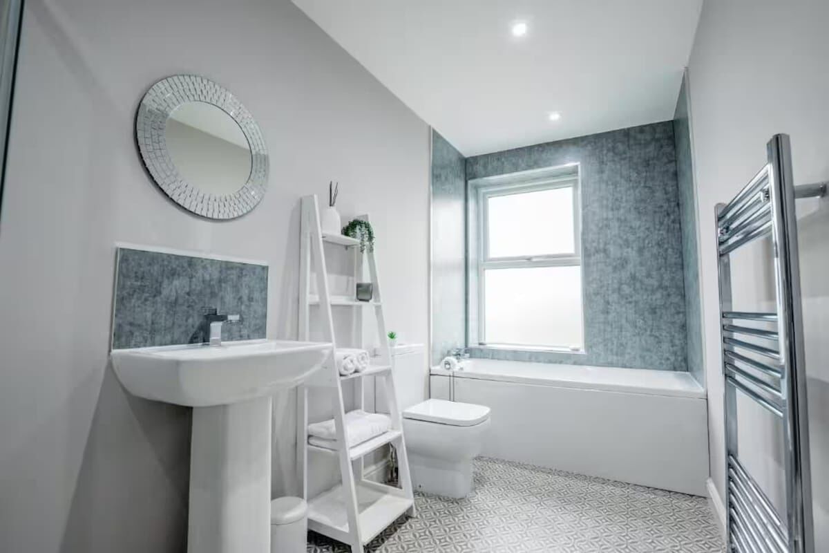 Een moderne badkamer met een wit wastafelmeubel, een ronde spiegel, een wit toilet en een bad.